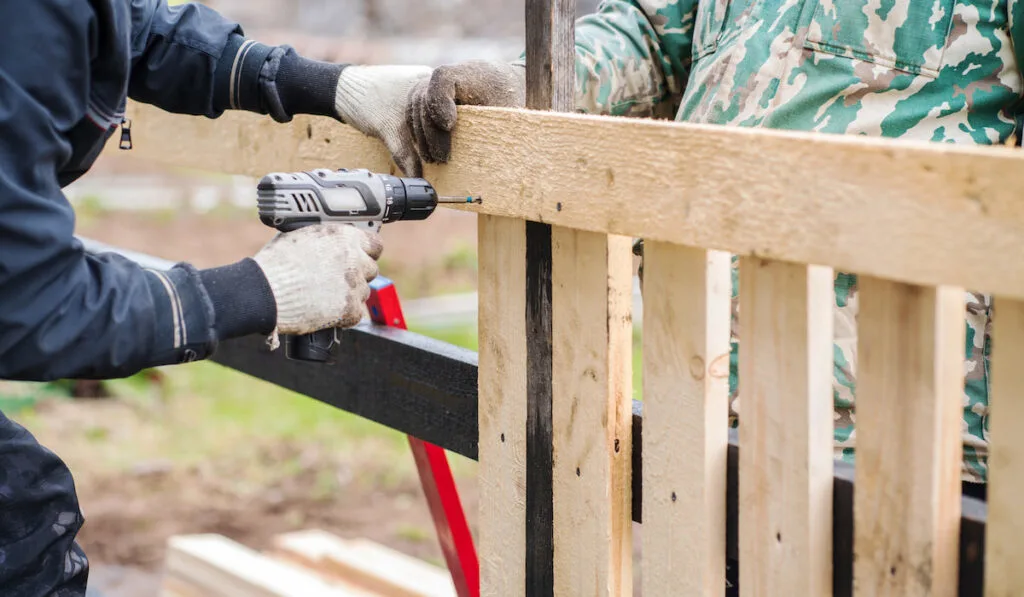 Two men in work clothes are building a fence for their house