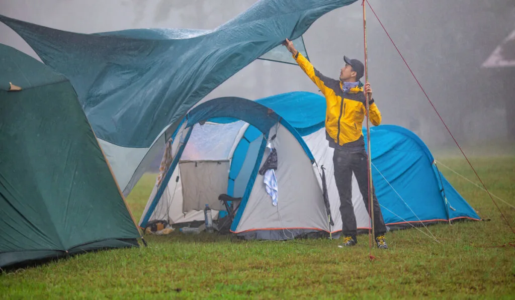 Man setting up tent while raining 