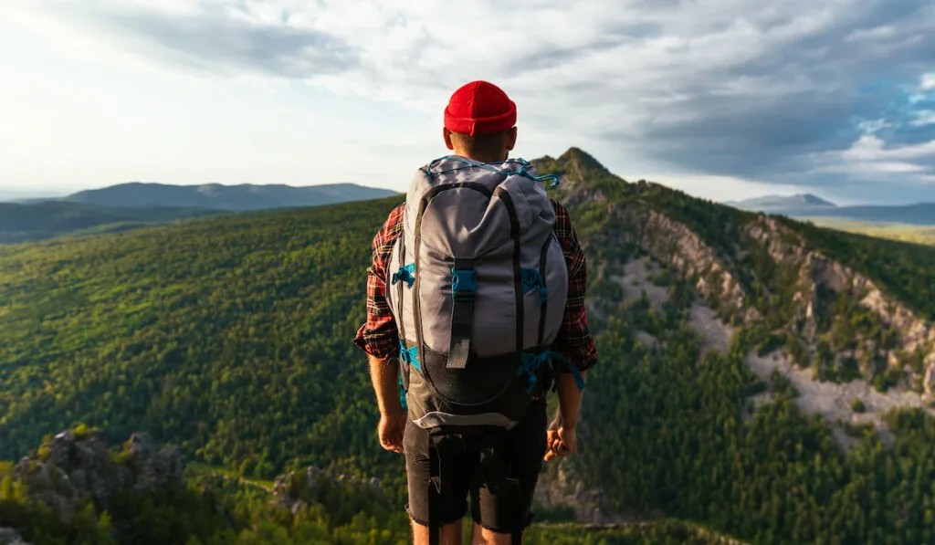 A tourist with a backpack is standing on the top of the mountain
