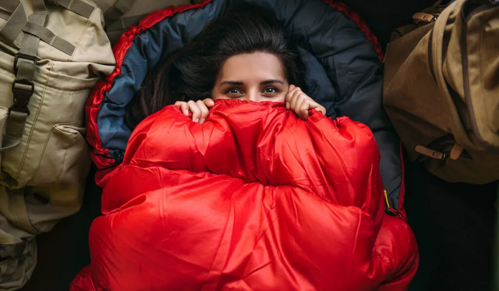 A young woman in a comfortable sleeping bag in a tent, top view.