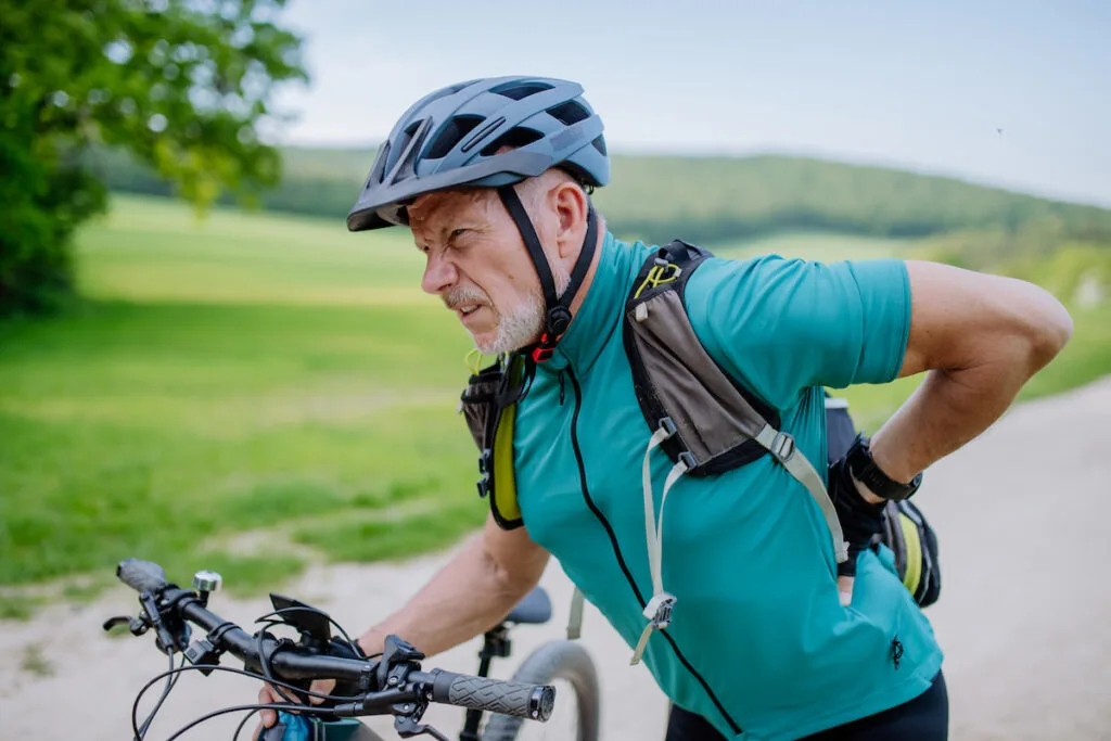 Active senior man in sportswear suffering from pain in his back after cycling,