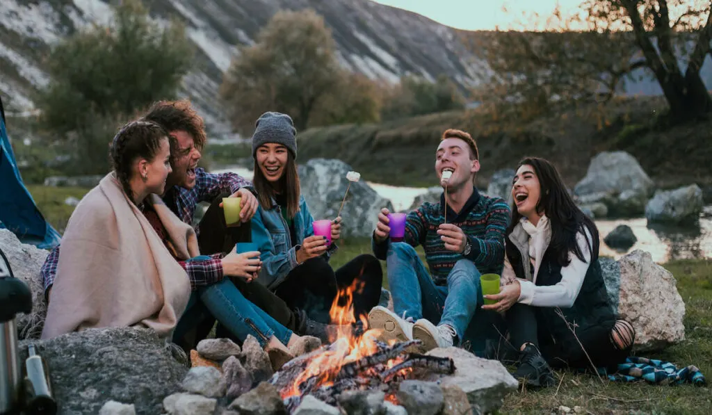 Camping time for group of friends sitting beside the fireplace and enjoying the time together in the middle of nature 