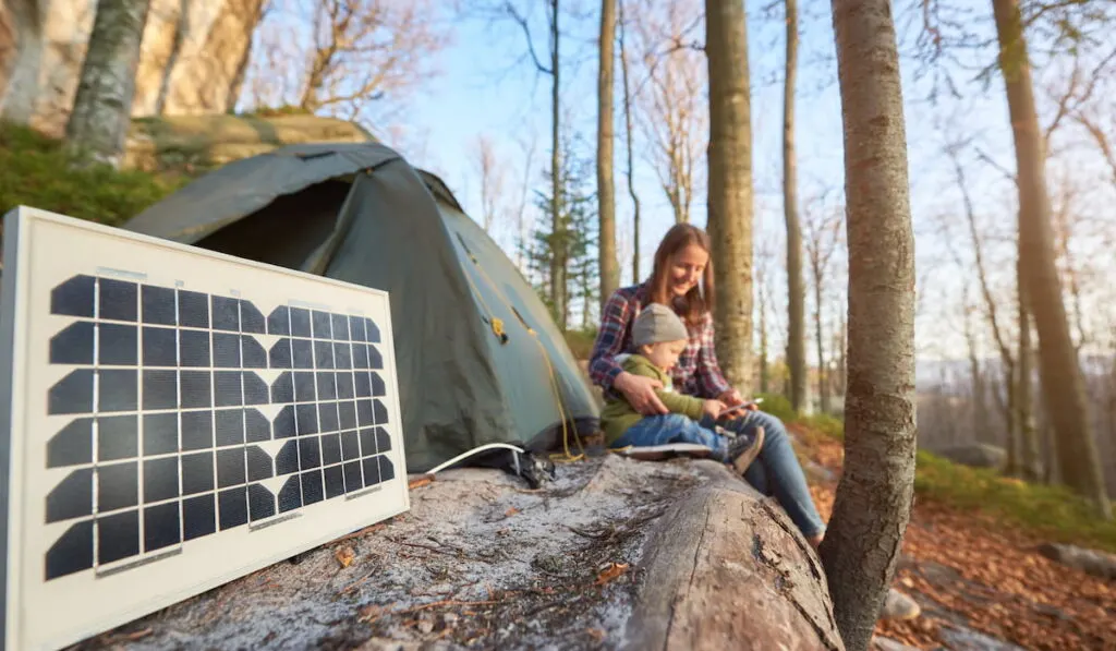 Close up solar battery in campsite on sunny autumn day against the background of young family