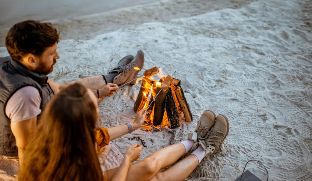 Couple cooking sausages at the campfire, camping near beach