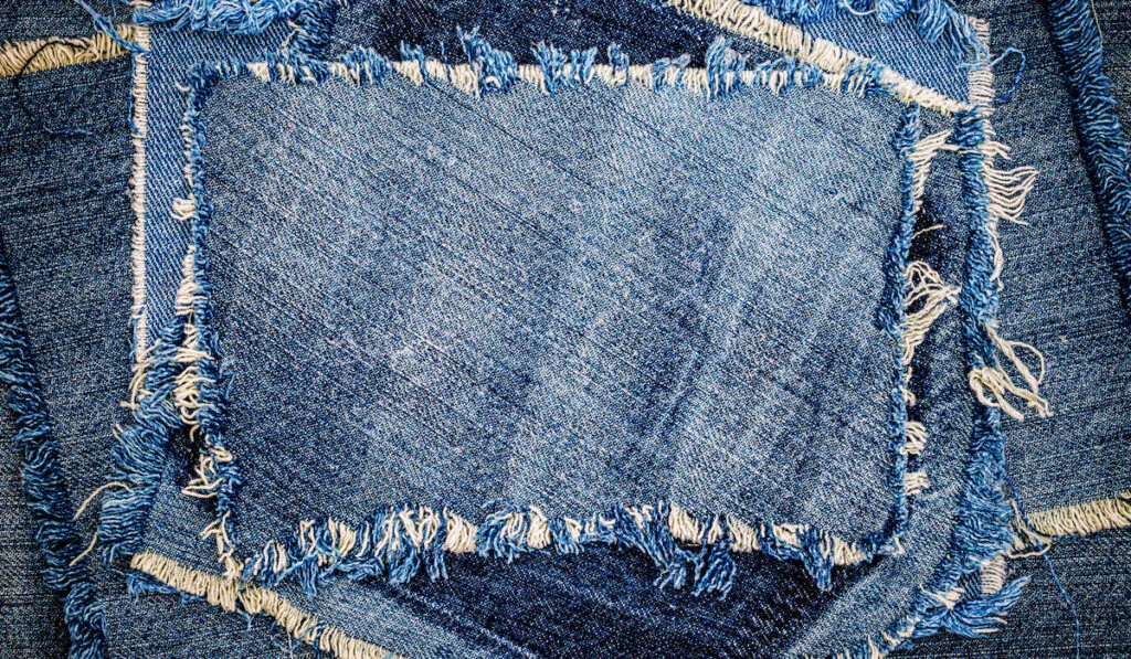 Destroyed torn denim blue jeans fabric patches on canvas background