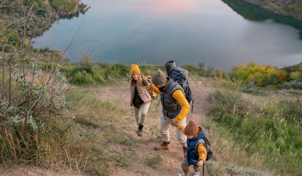 Family of hikers with backpacks climbing mountain against river camping activity