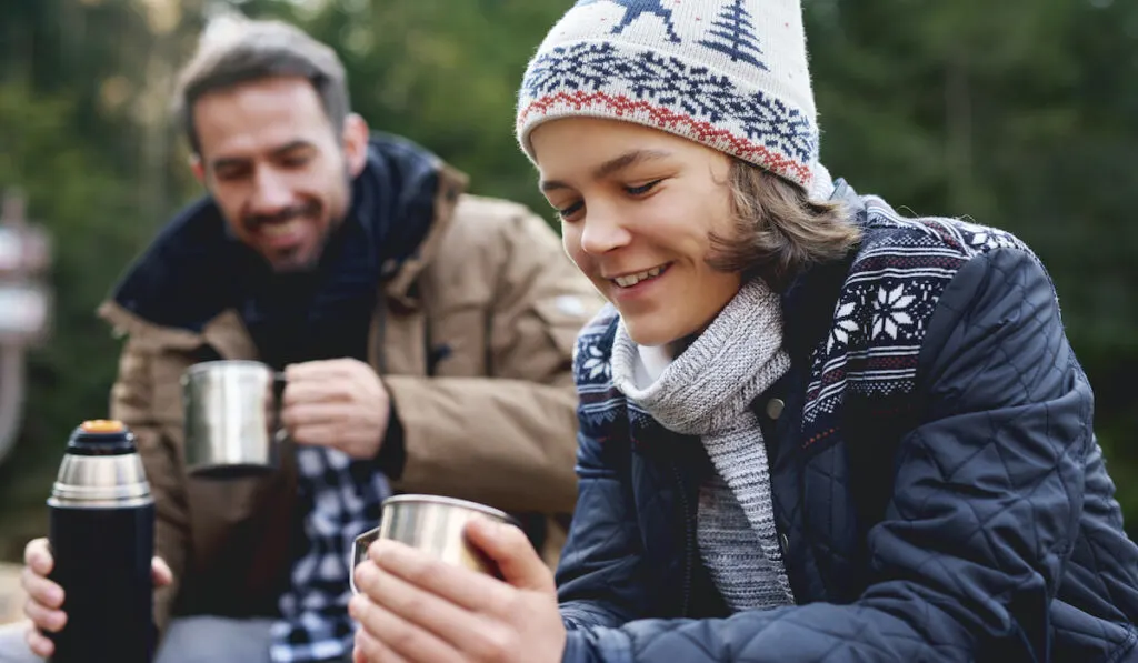 Father and son drinking tea in the forest resting while hiking 