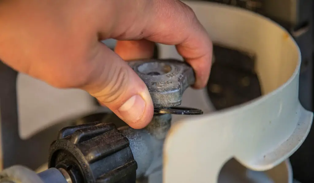 Hand turning on gas propane grill tank knob close up grilling off twisting