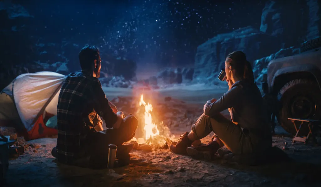 Happy Couple Sitting by Campfire Watching Night Sky while Camping