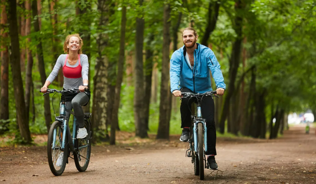 Happy couple riding bicycle down forest road