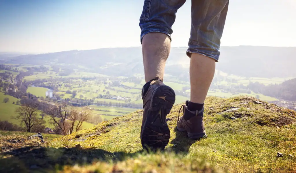 Hiker hiking on a mountain trail with distant views of countryside in summer sunshine