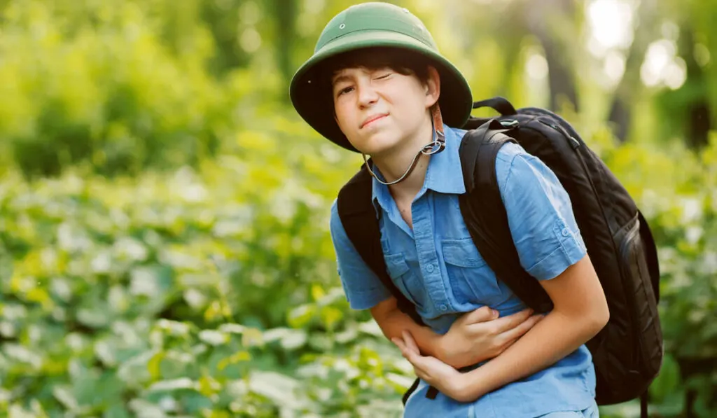 Little boy traveler in the forest suffering from stomach ache 