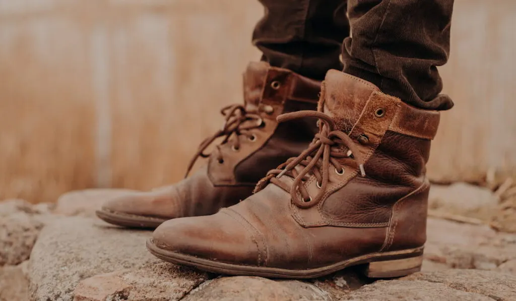 Man in brown old leather boots and trousers stands on stones against blurred background