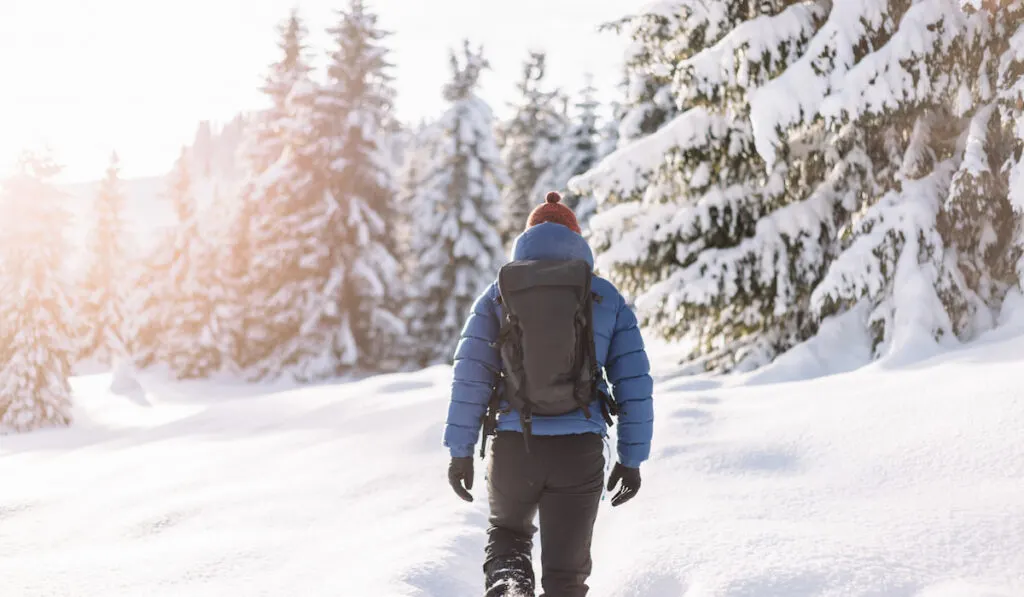 Man on a hike in the snow during winter wearing thermal jacket with hood