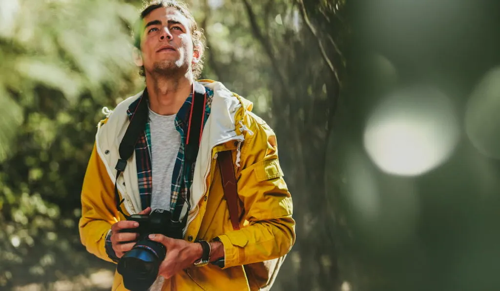 Portrait of a man wearing jacket and backpack walking in a forest holding a dslr camera