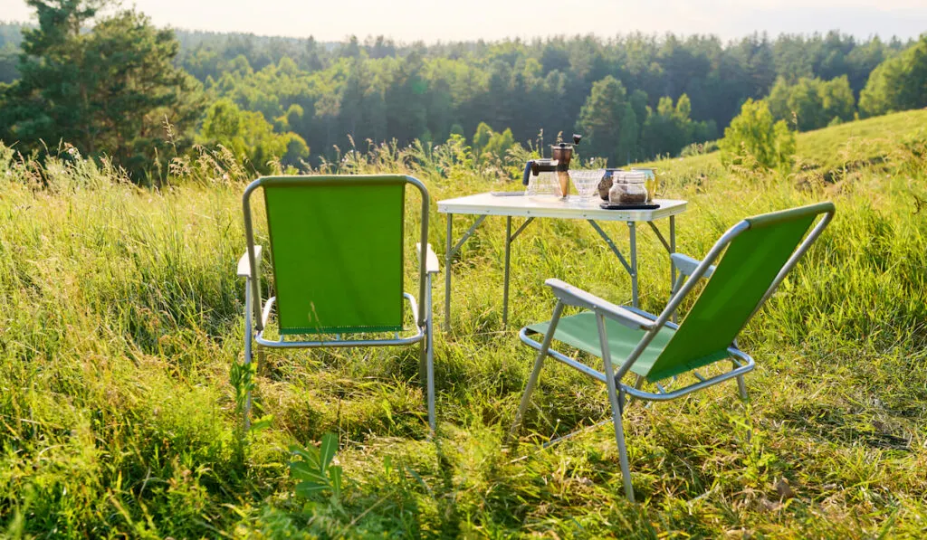 Set of folding furniture for camping, table and chair, summer nature of wild meadow
