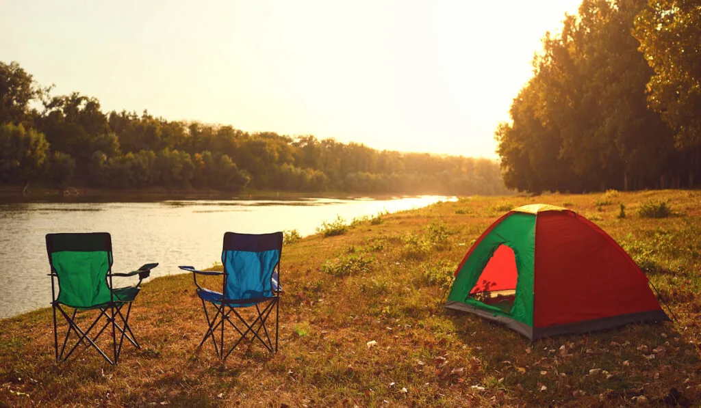 Tent and chairs by the lake at sunset in summer in autumn.
