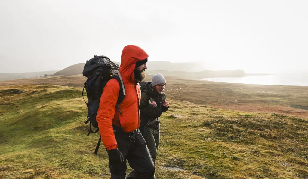 Two men walking with rucksacks, hiking across open ground

