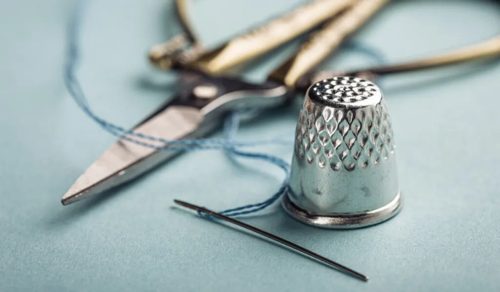 Vintage silver metal thimble and needle, scissors on blue background

