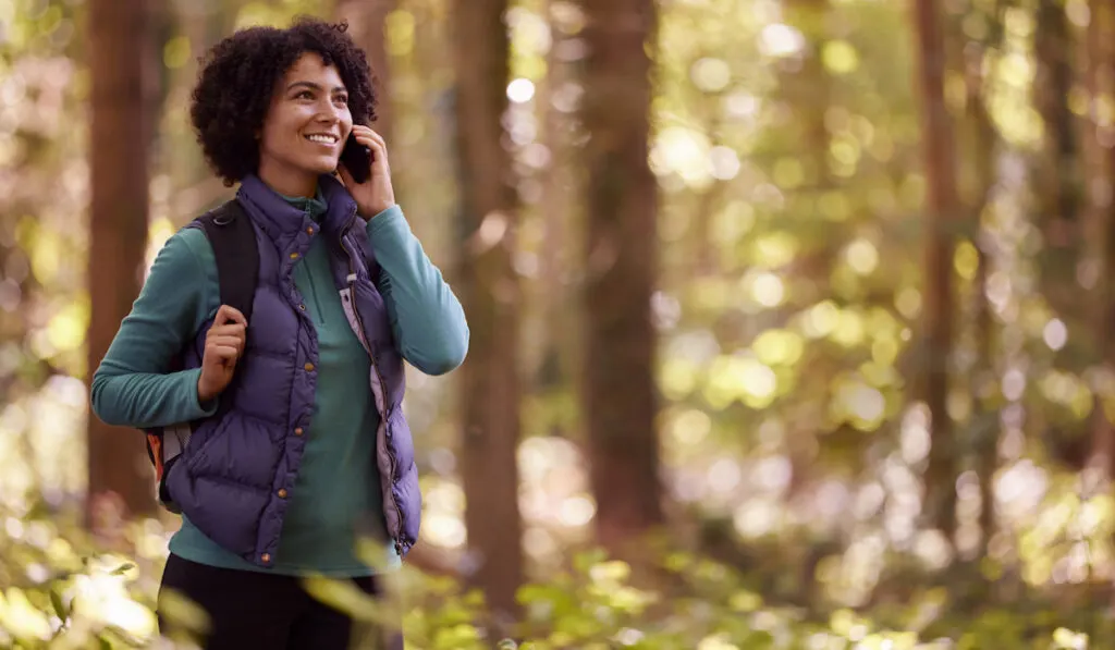 Woman On Hike Through Forest Talking On Mobile Phone

