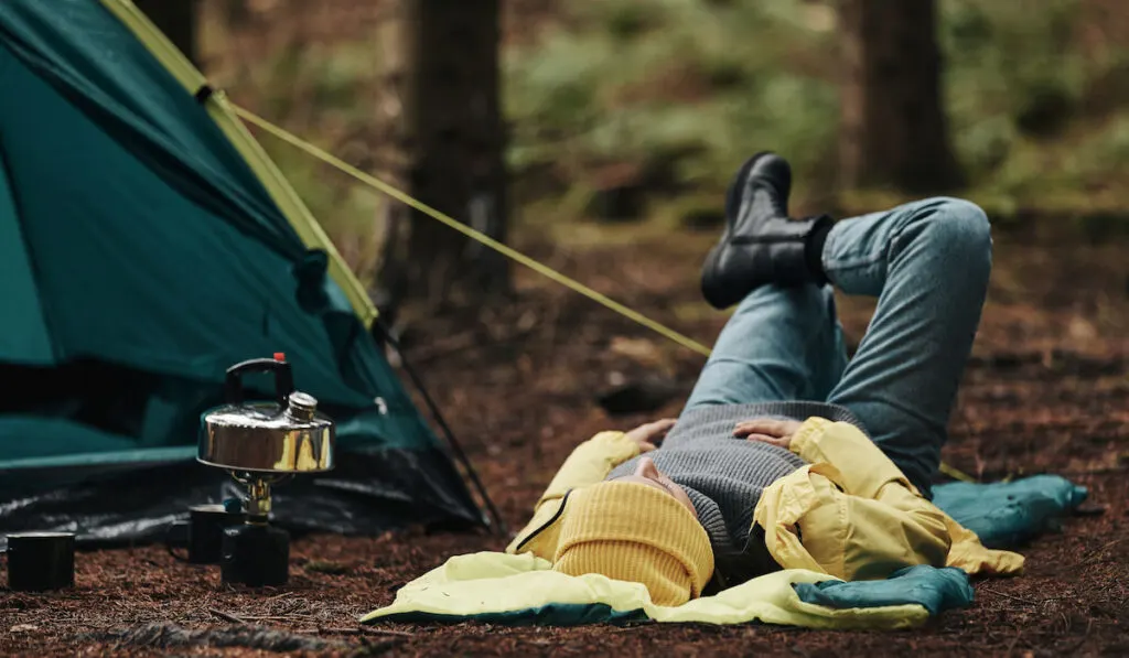 Woman-in-hiking-gear-lying-on-her-sleeping-bag-at-her-campsite
