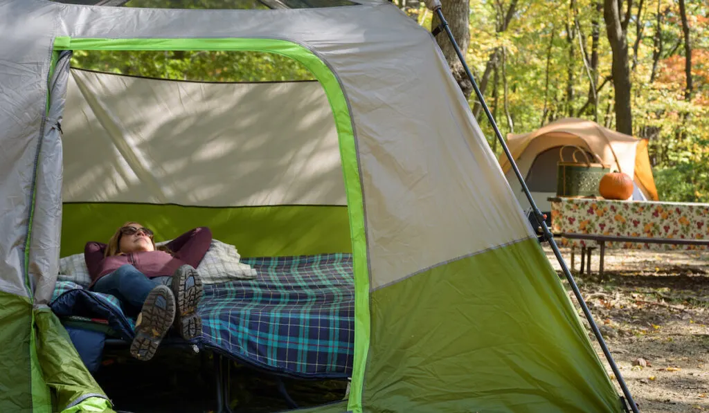 Woman laying on cot in tent relaxing on fall camping trip 