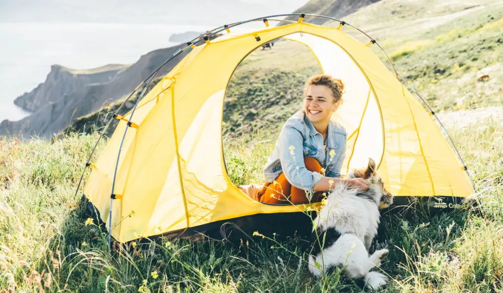 Woman resting with a dog on the seashore view from a tent 