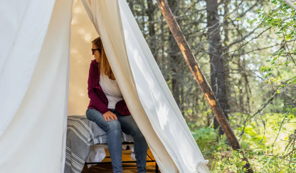 Woman sitting on cot inside tipi at campground. 