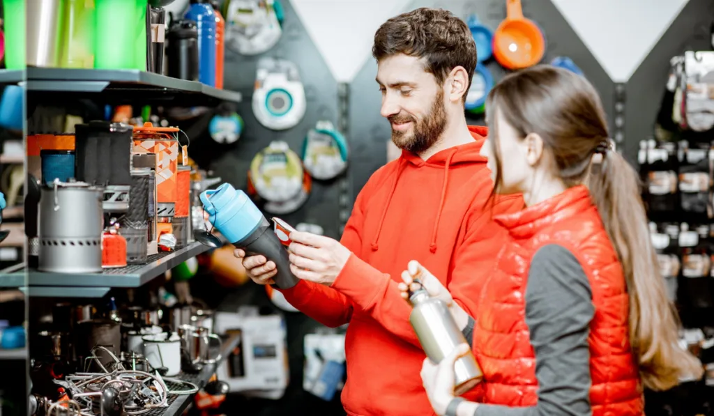Young couple dressed in red sportswear choosing dishes for camping in the shop with travel equipment