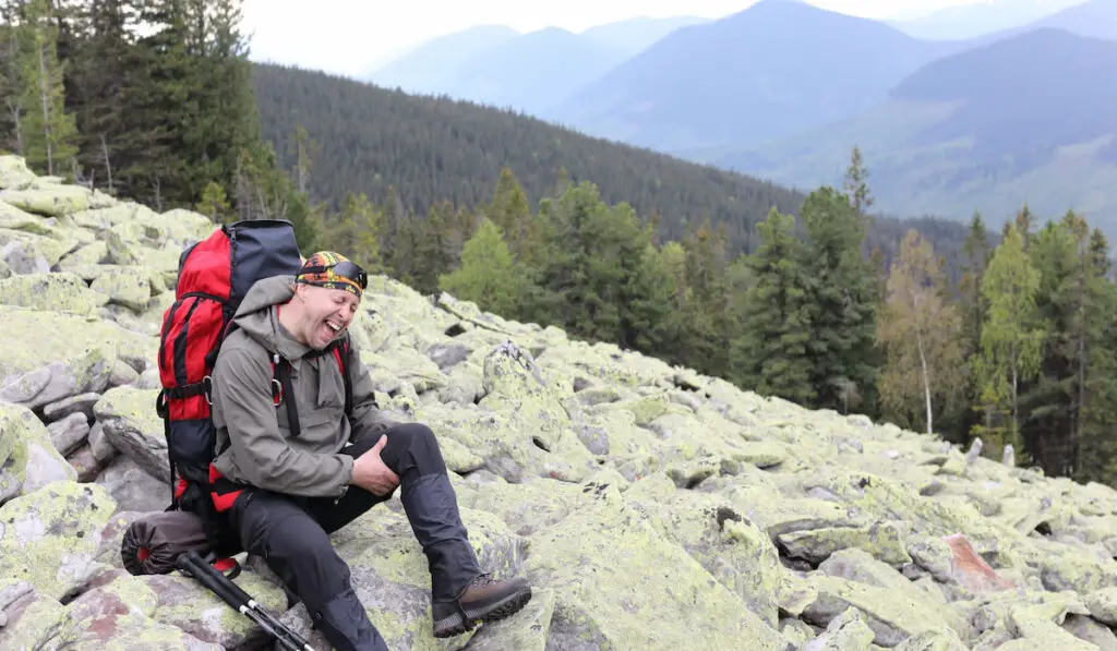 injured hiker siting on rocks in the mountains and screams due to pain holding his feet