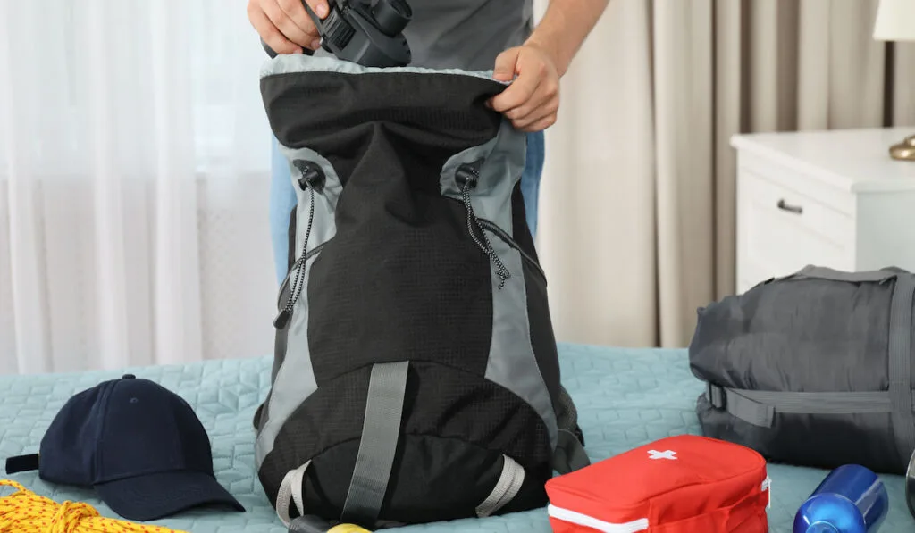 man preparing camping equipment, rope flashlight first aid kit on his bag 