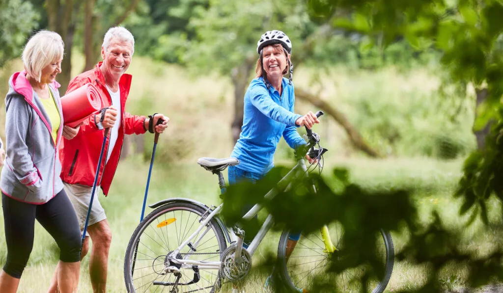 two seniors on hiking stick and a woman with her bicycle 