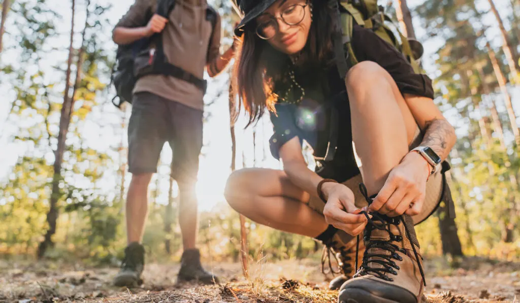 woman tying hiking boot outdoors on trail in forest with his boyfriend