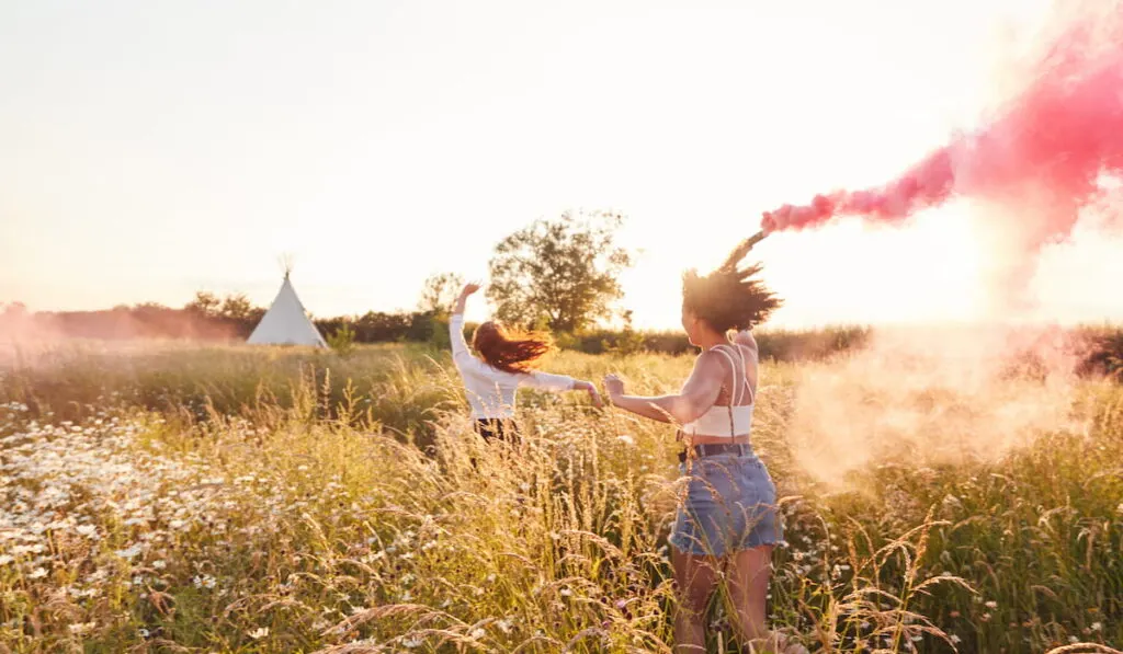 Two Female Friends Camping running with smoke flares