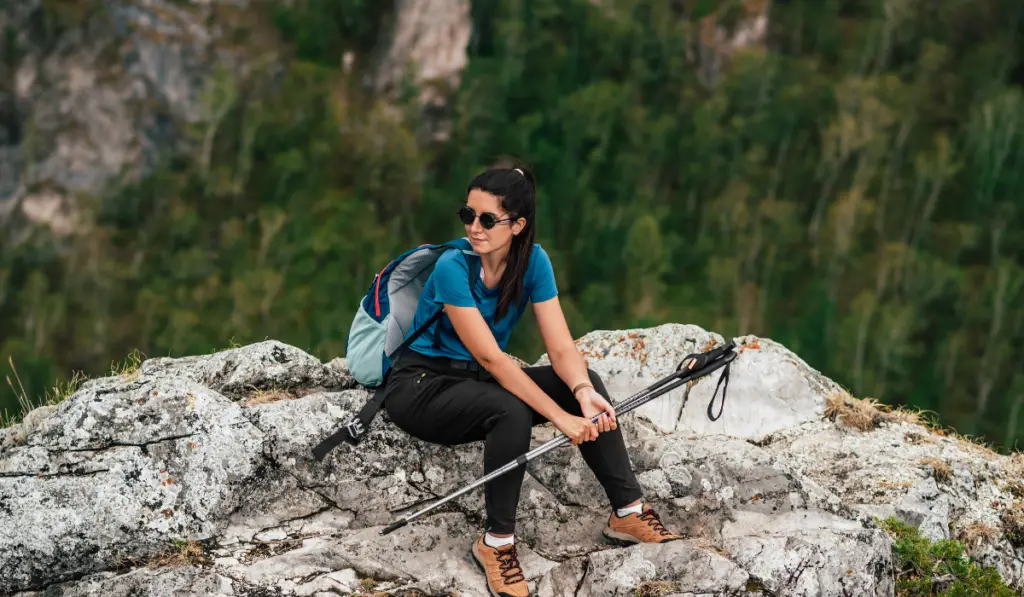 Woman hiker with trekking poles and backpack on a top of a mountain.