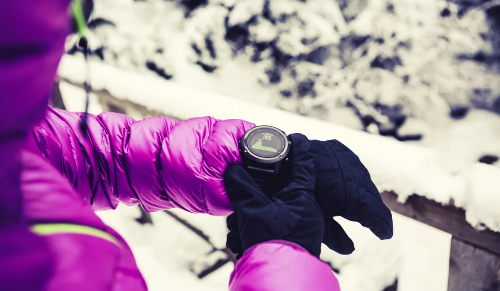 Woman hiker checking sports watch in winter woods and mountains
