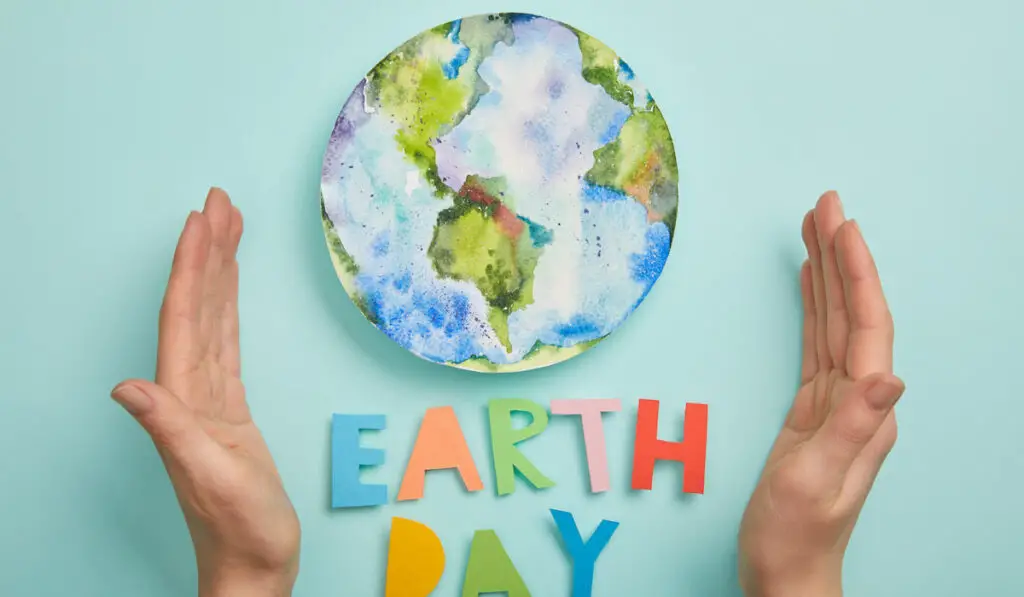 Top view of a hand and colorful paper letters as earth day and plant picture on turquoise background