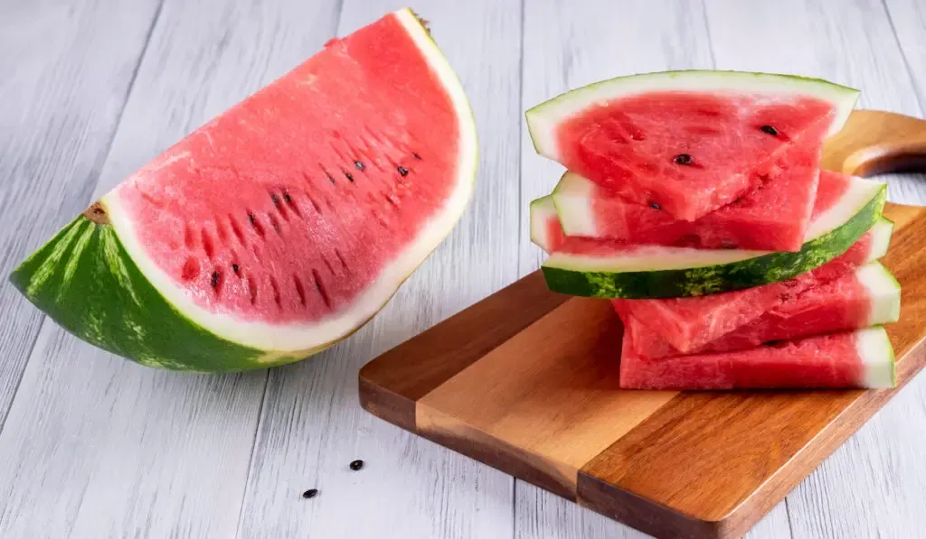 A portion of a ripe watermelon cut and slices on wooden table