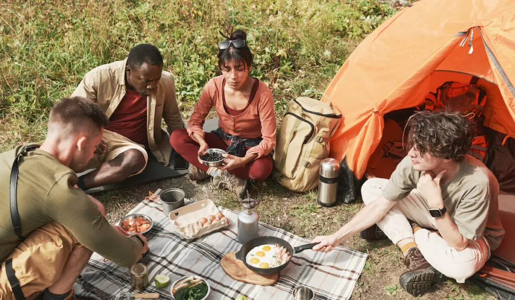Young hikers cooking eggs on burner
