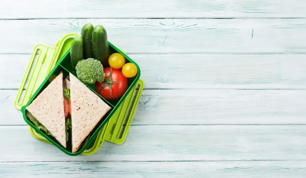 container box with vegetables and sandwich on wooden background